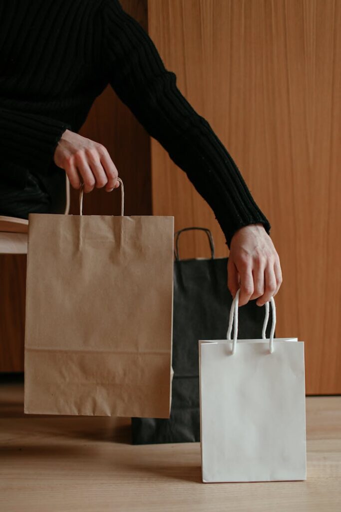 Person holding brown and white paper shopping bags indoors, focusing on minimalistic lifestyle.