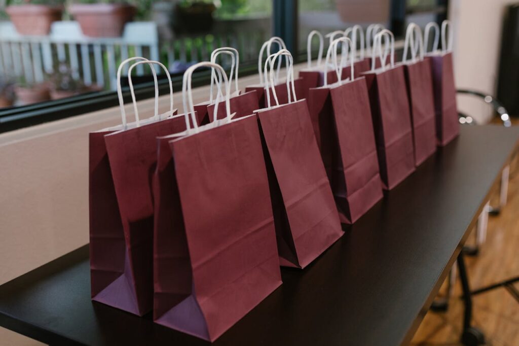 Purple paper bags with handles lined up on a table indoors, perfect for events.